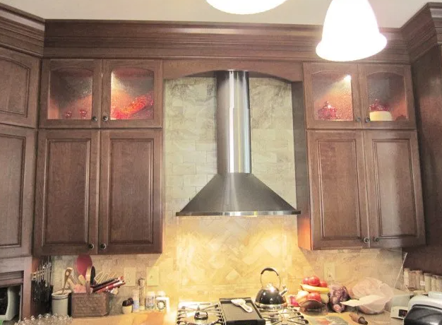 Kitchen cabinets flanking a stainless steel range hood above a stovetop, with warm lighting.