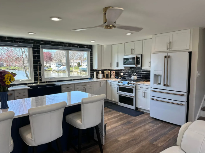 Modern kitchen with white cabinets, blue island with bar stools, and a view of a lake through a window.