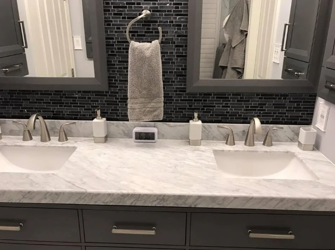 Double bathroom vanity with gray cabinets, marble countertop, black tile backsplash, and silver fixtures.