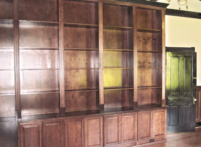 Built-in wooden bookshelves with closed cabinet storage below; dark brown color; in a room with a door.