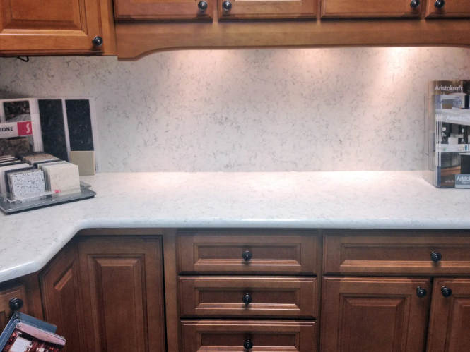 Kitchen countertop with speckled white surface, wooden cabinets, and under-cabinet lighting.