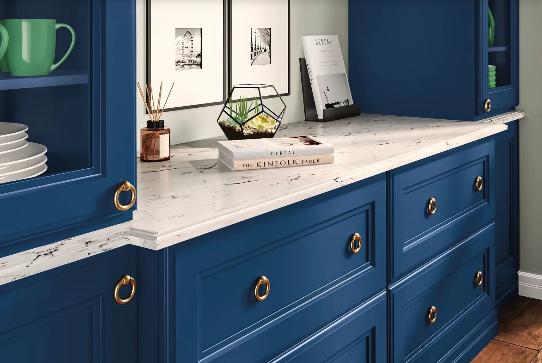 Blue kitchen cabinets with gold hardware and white speckled countertop.
