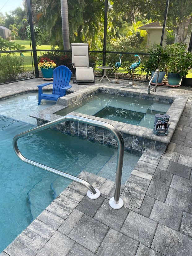 Backyard pool with hot tub, blue chair, lounge chairs, and patio stones beside a garden.