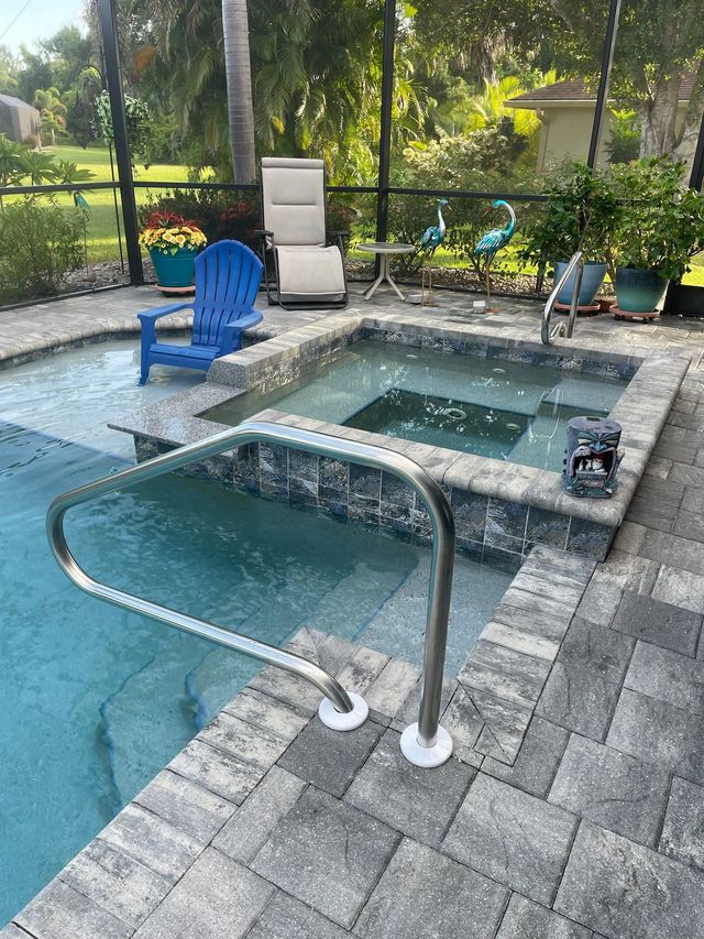 Backyard pool with hot tub, blue chair, lounge chairs, and patio stones beside a garden.