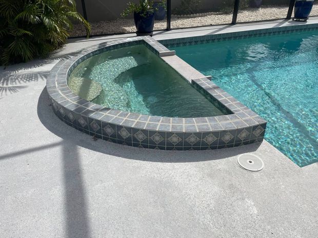 Curved stone pool spa with blue water beside a bright white patio.