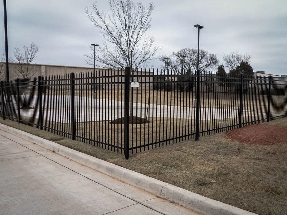 Black metal fence around a concrete utility area beside a sidewalk and road under a cloudy sky
