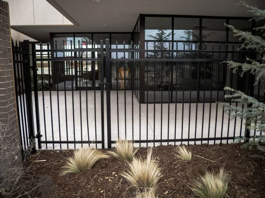 Black metal fence and gate in front of a building entrance with patio and desert plants