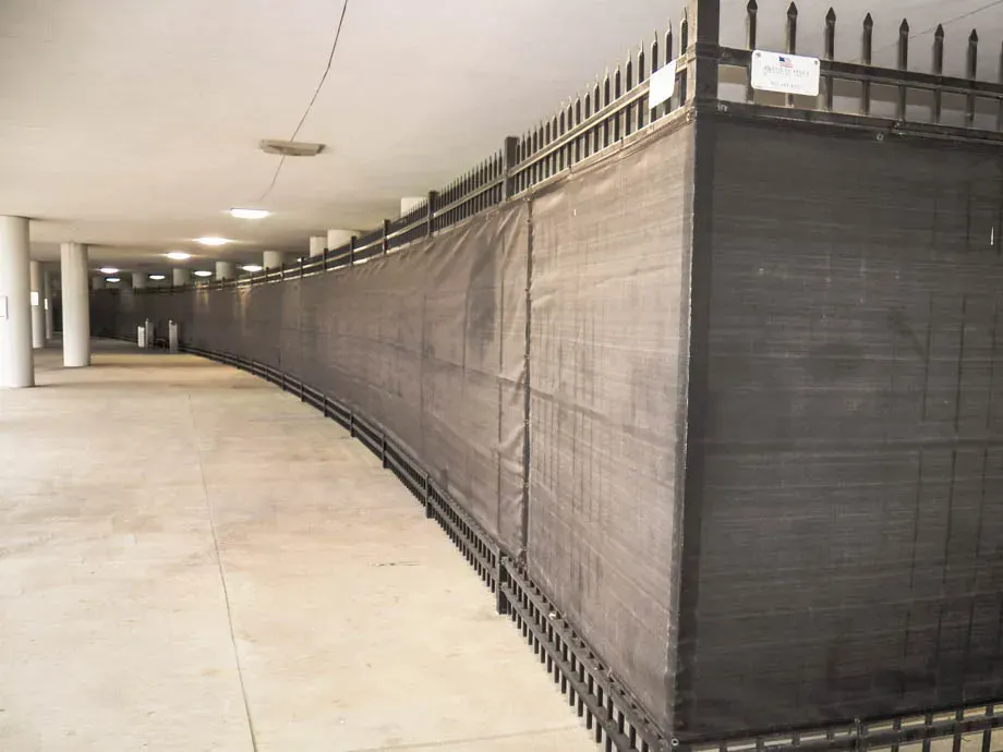 Long indoor hallway with a black mesh barrier lining the right side and concrete floor