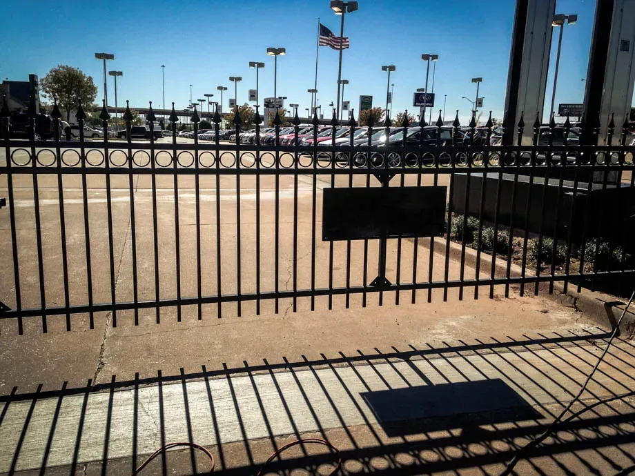 Black metal gate at a sunny parking lot entrance with tall light poles in the background