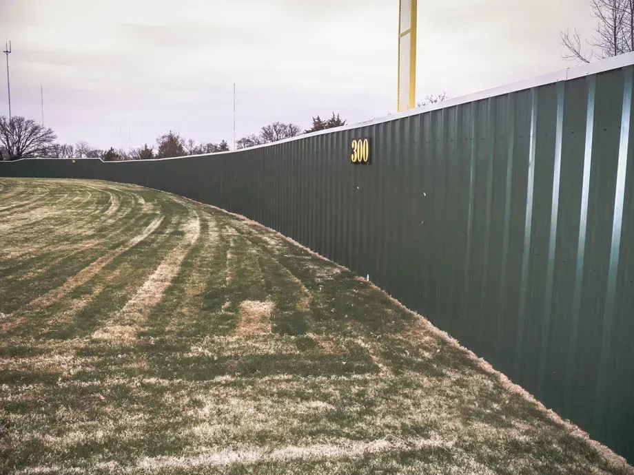 Curved grassy berm beside a long dark green metal fence under an overcast sky