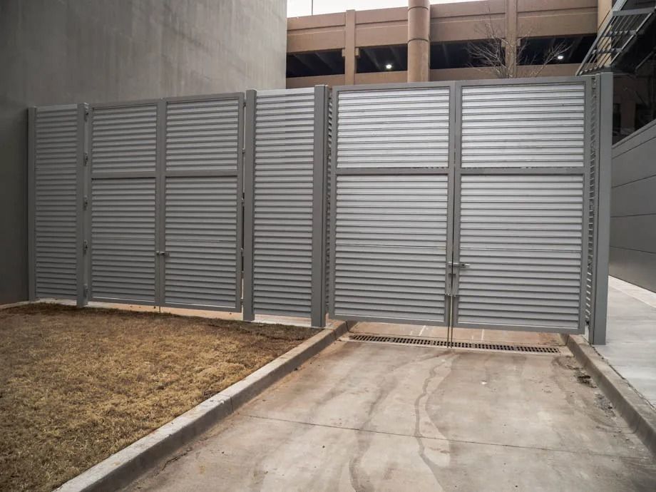 Gray metal gate blocking a concrete driveway beside a dry grassy yard