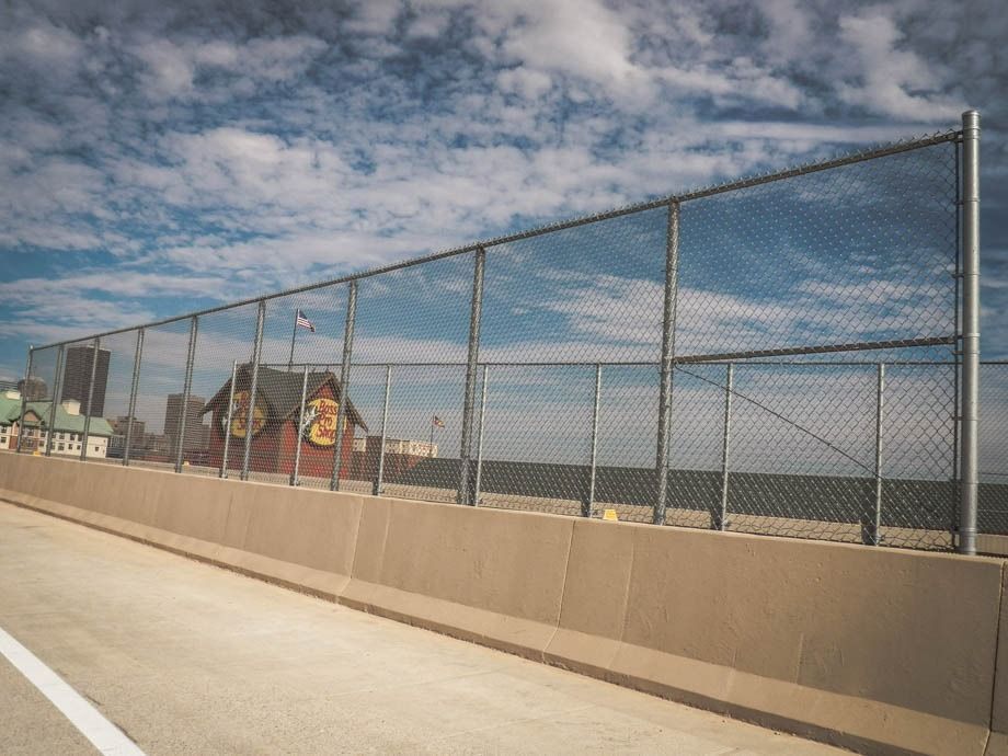 Chain-link fence along a sidewalk with a cloudy sky and distant ocean view