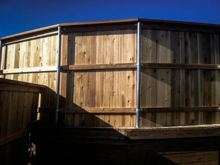 Wooden fenced enclosure with curved panels and a blue roof under clear sky