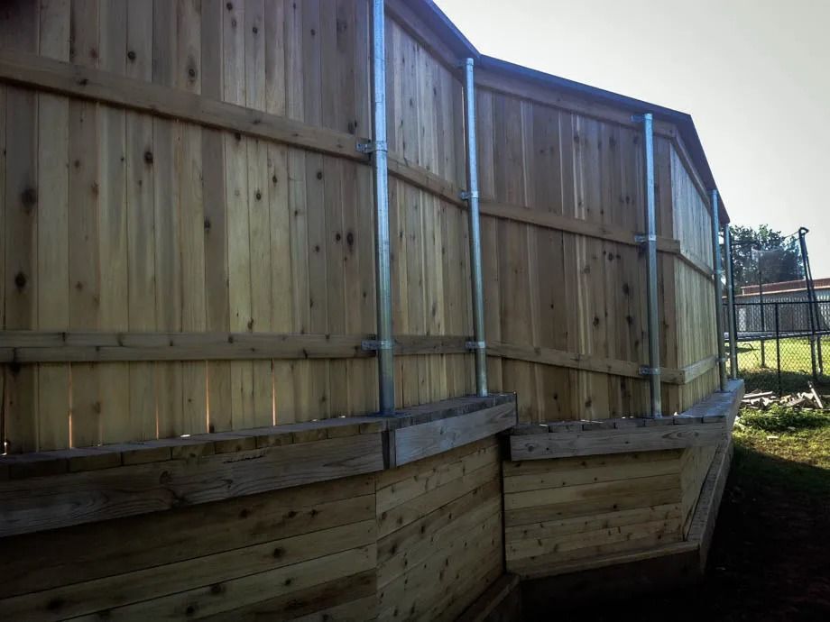 Wooden raised garden beds beside a tall wooden fence in a sunny yard
