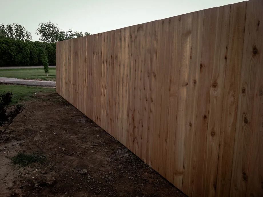 Long wooden fence along a dirt path beside a grassy field under an overcast sky