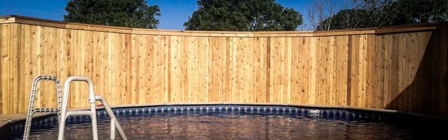Backyard pool with wooden privacy fence, blue tile edge, and a ladder on the left
