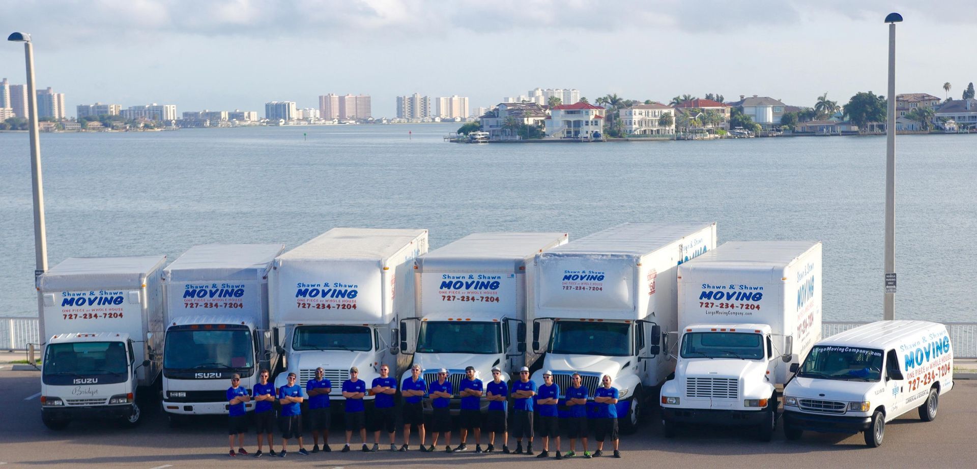 Group of movers standing in front of moving trucks and a body of water.