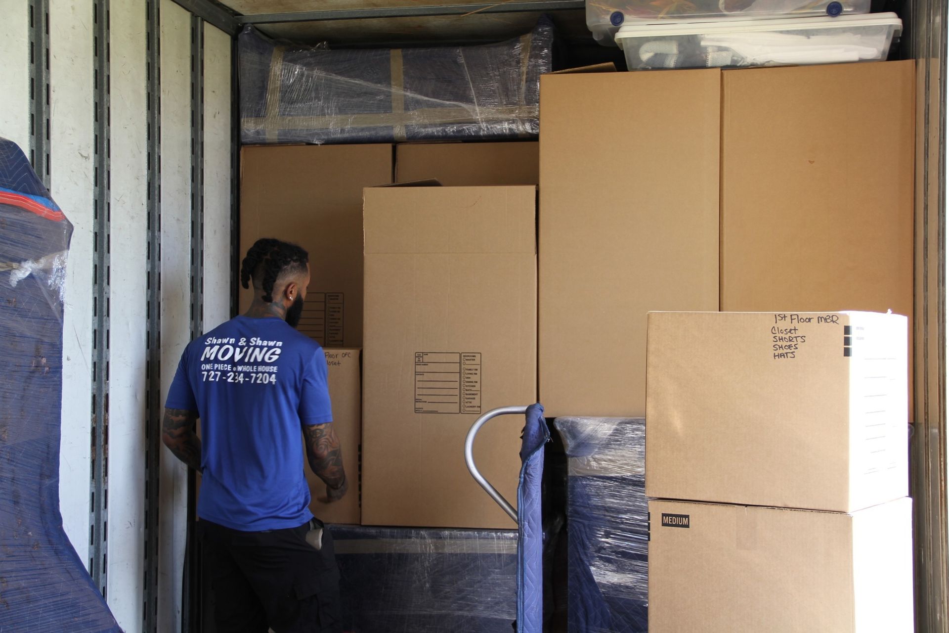 Man in blue shirt packing boxes into a moving truck.