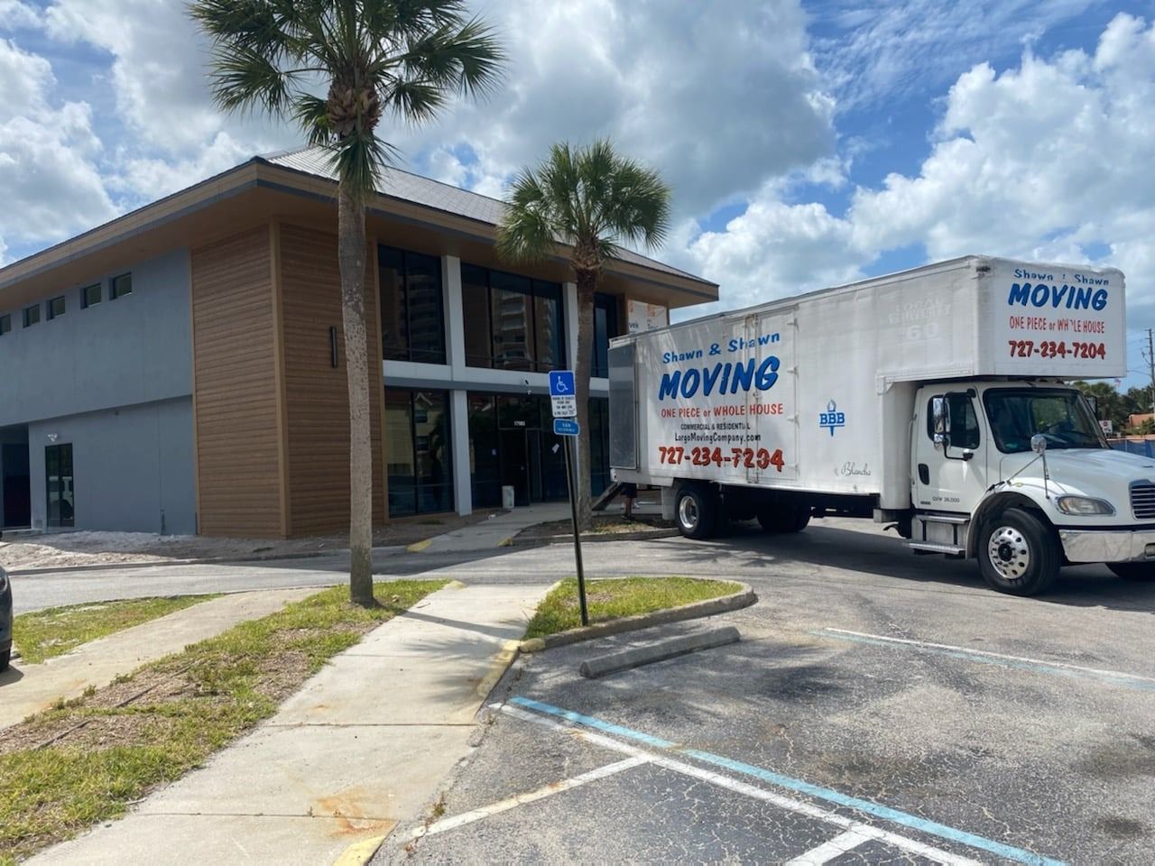 Moving truck parked in front of a building with accessible parking sign; sunny day.