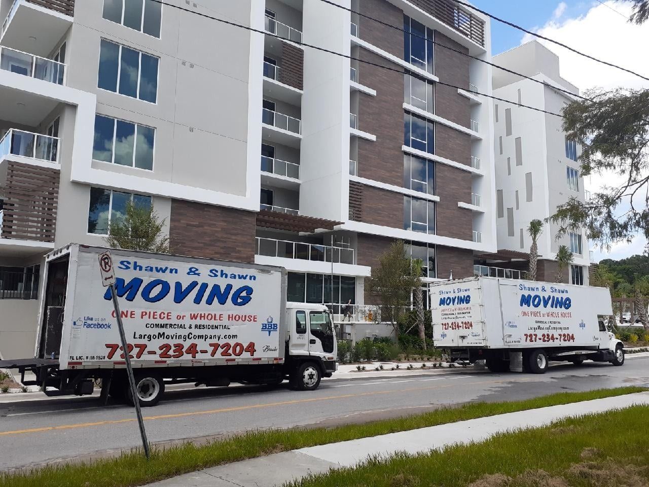 Two moving trucks parked in front of a modern apartment building, the trucks are labeled 