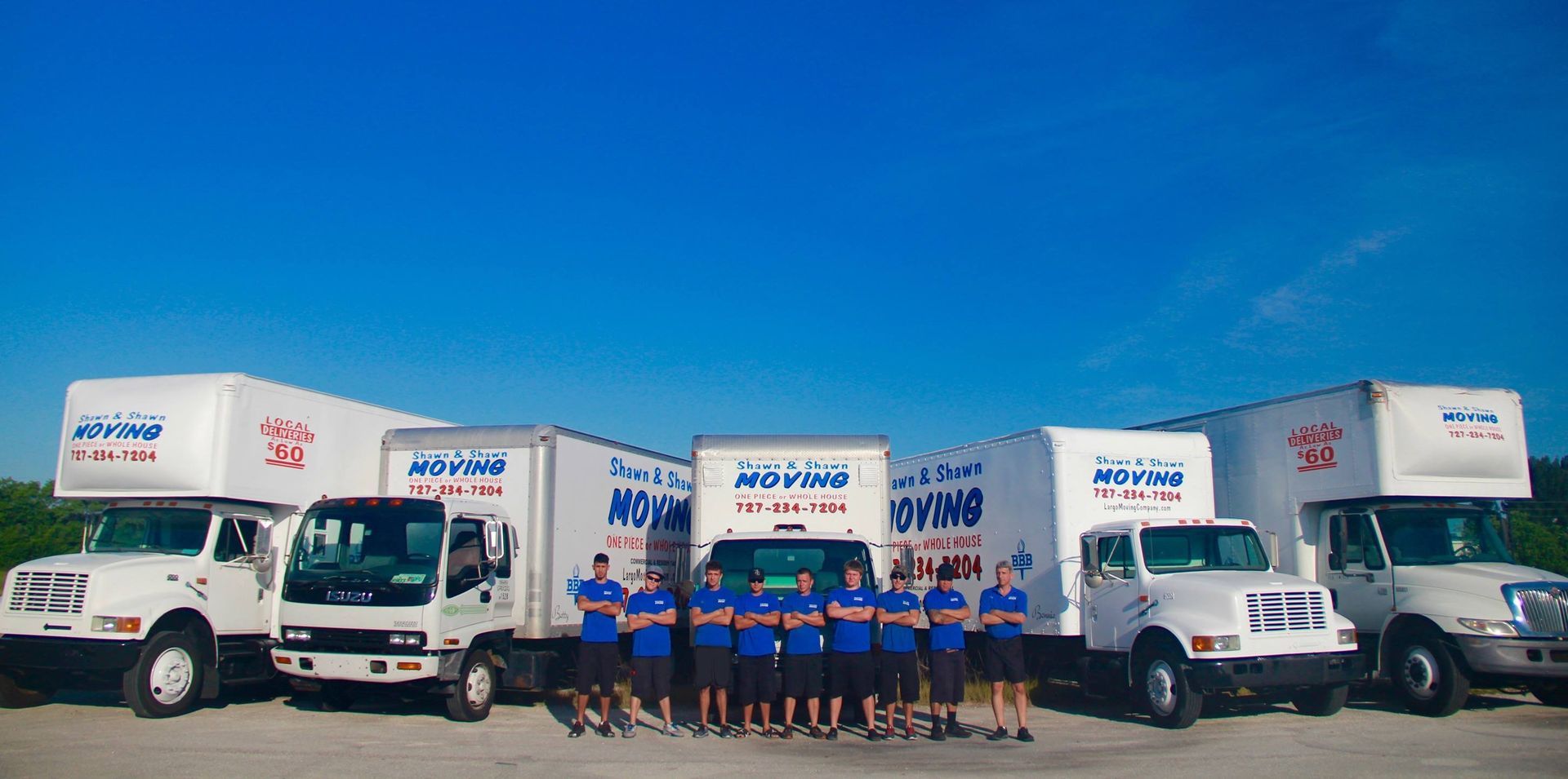 Movers standing in front of several white moving trucks under a bright blue sky.