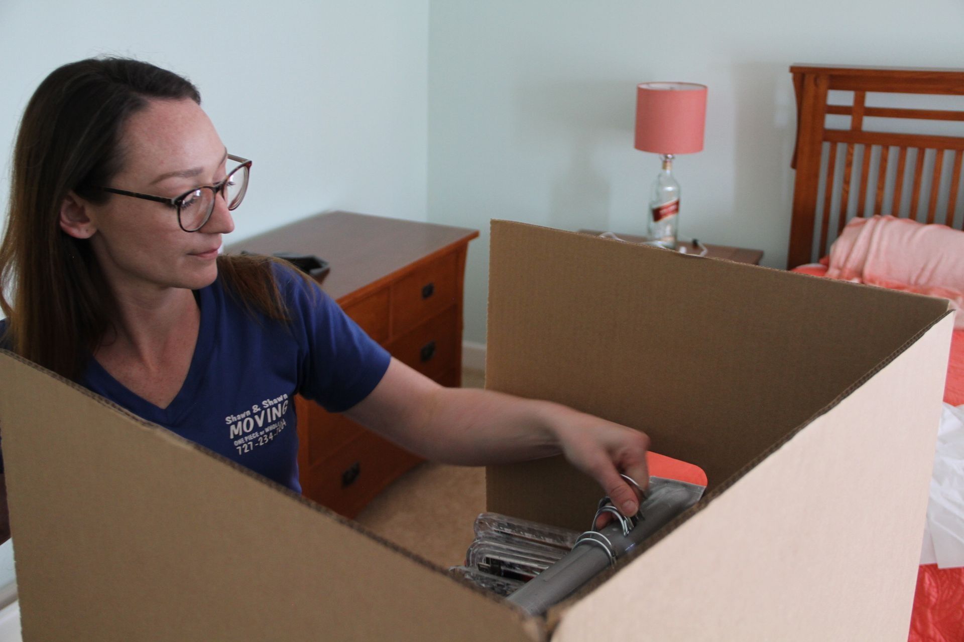 Woman packing a box in a bedroom with dresser and bed.