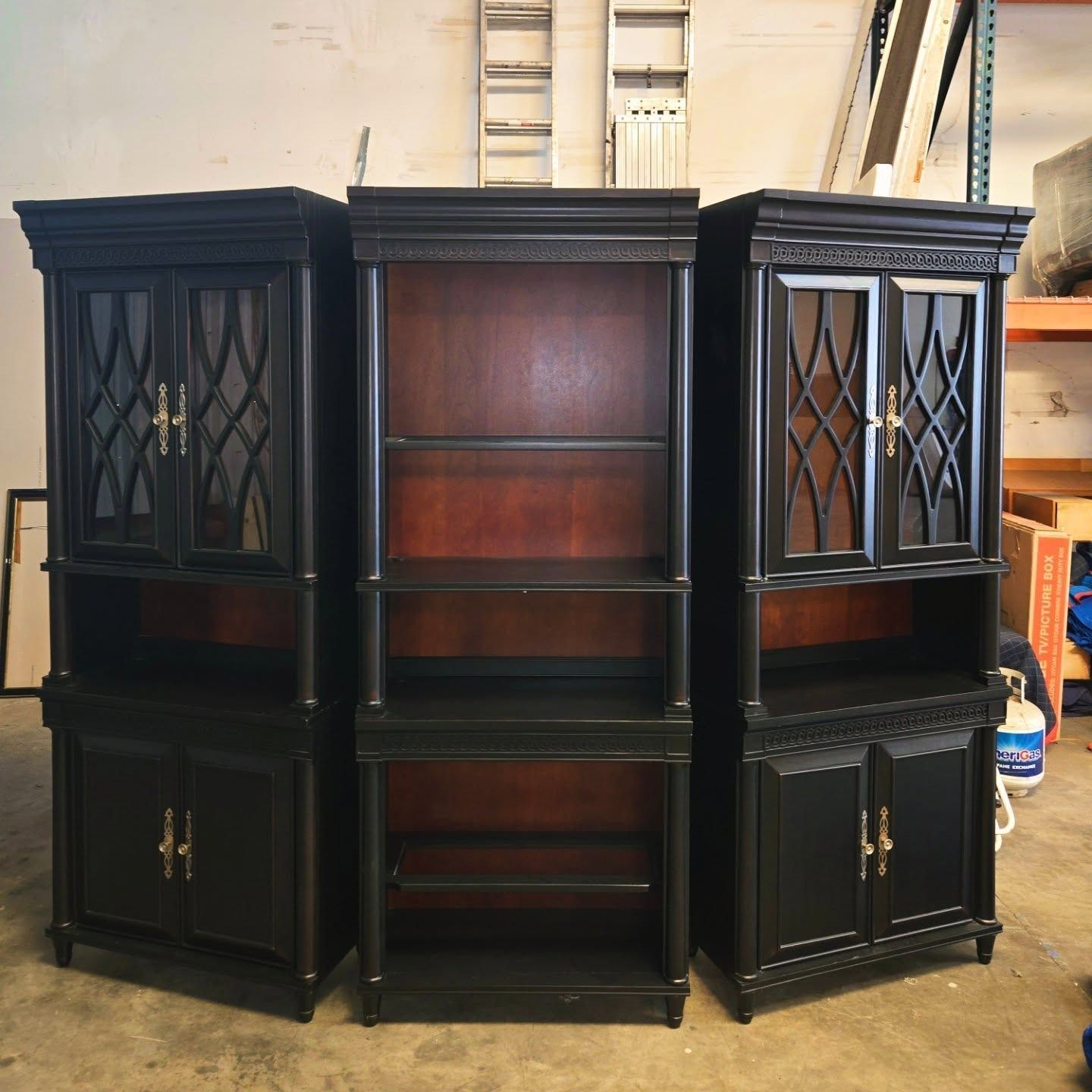 Three black bookshelves with interior shelving against a wall.