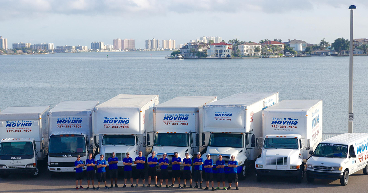 Moving company team posing with trucks near water and city skyline.