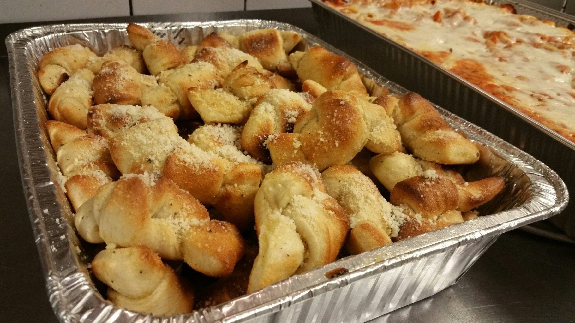 A pan of garlic knots next to a pan of lasagna