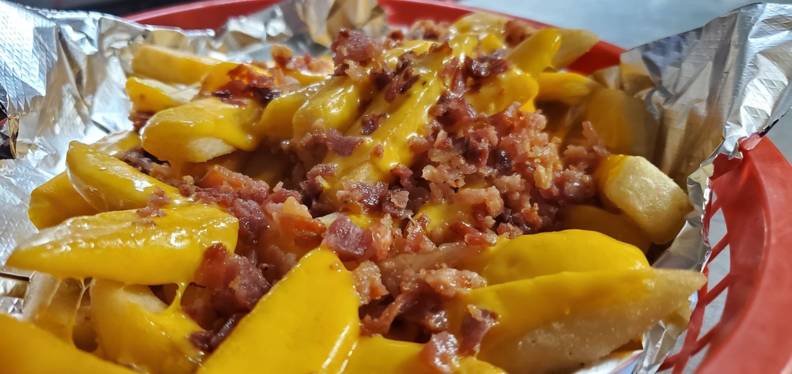 A close up of a basket of french fries with cheese and bacon.