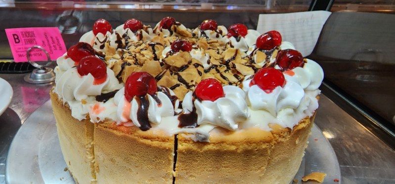 A cheesecake with whipped cream and cherries on top is on a plate.