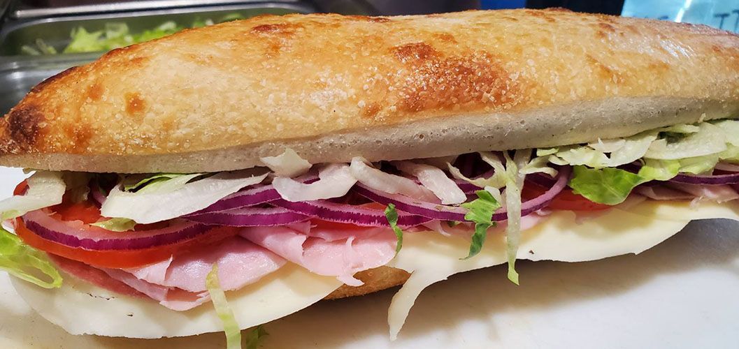 A sandwich with ham , cheese , lettuce , tomatoes and onions on a white plate.