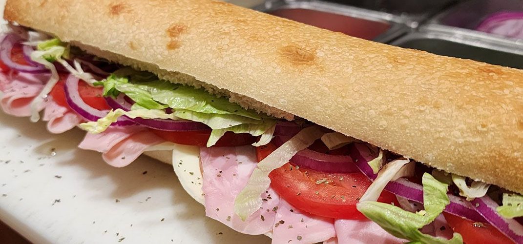 A sub sandwich with ham , lettuce , tomatoes and onions on a white plate.