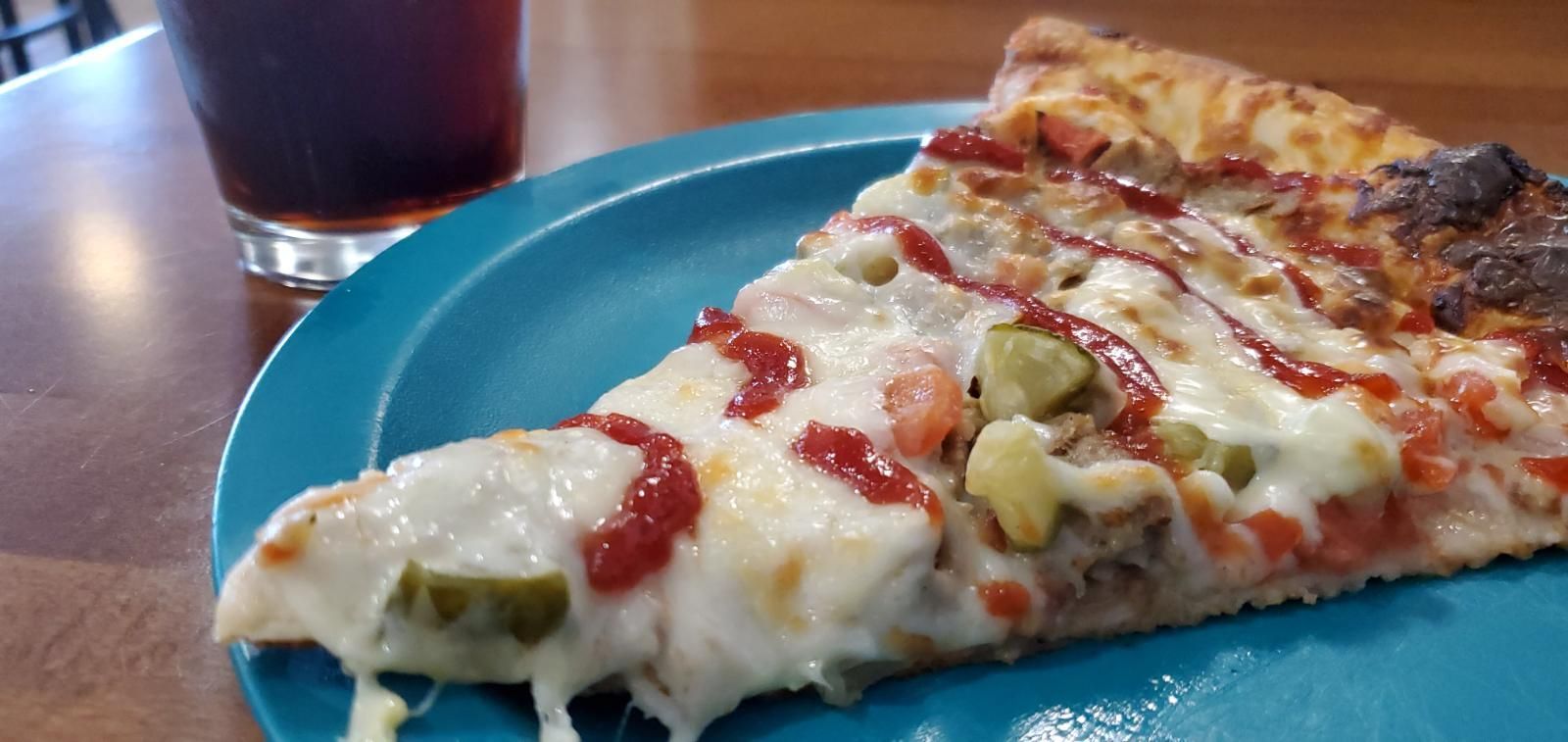 A slice of pizza is on a blue plate next to a glass of soda.