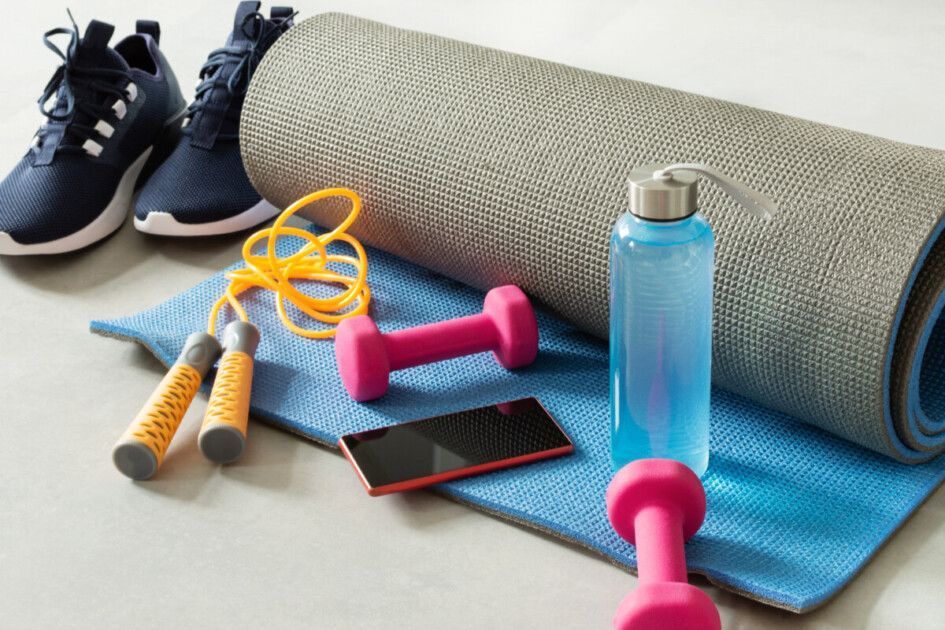 Fitness equipment: sneakers, yoga mat, dumbbells, jump rope, water bottle, and phone on a blue mat.