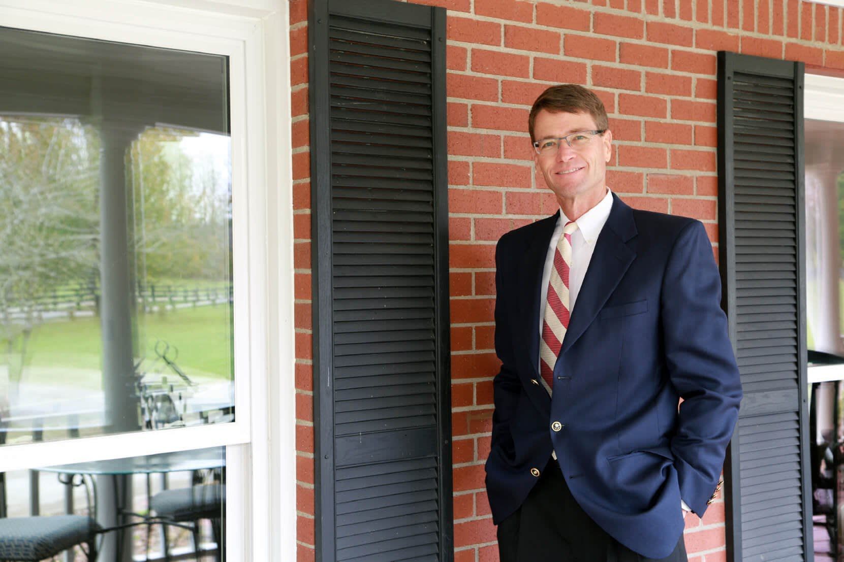 A man in a suit and tie is standing on a porch with his hands in his pockets