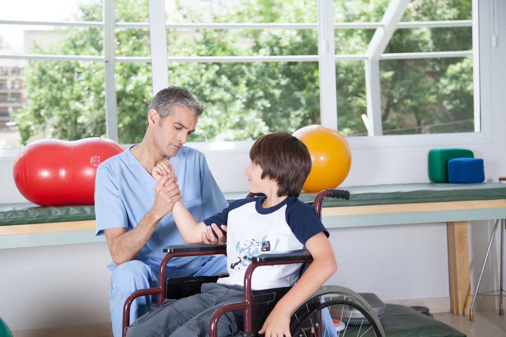 A young boy in a wheelchair is being helped by a nurse.
