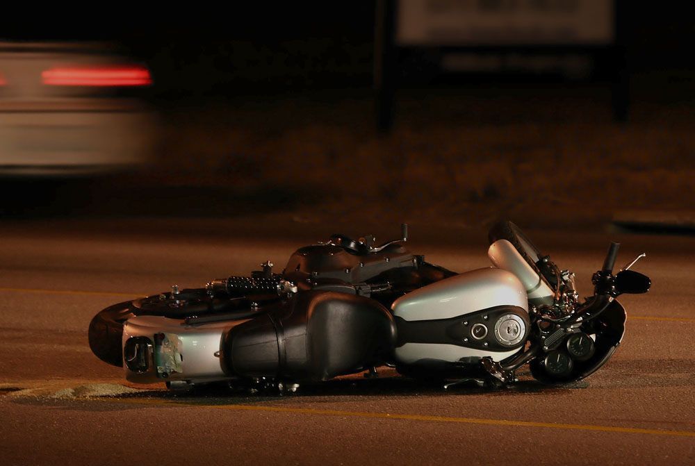 A motorcycle is laying on its side on the side of the road.