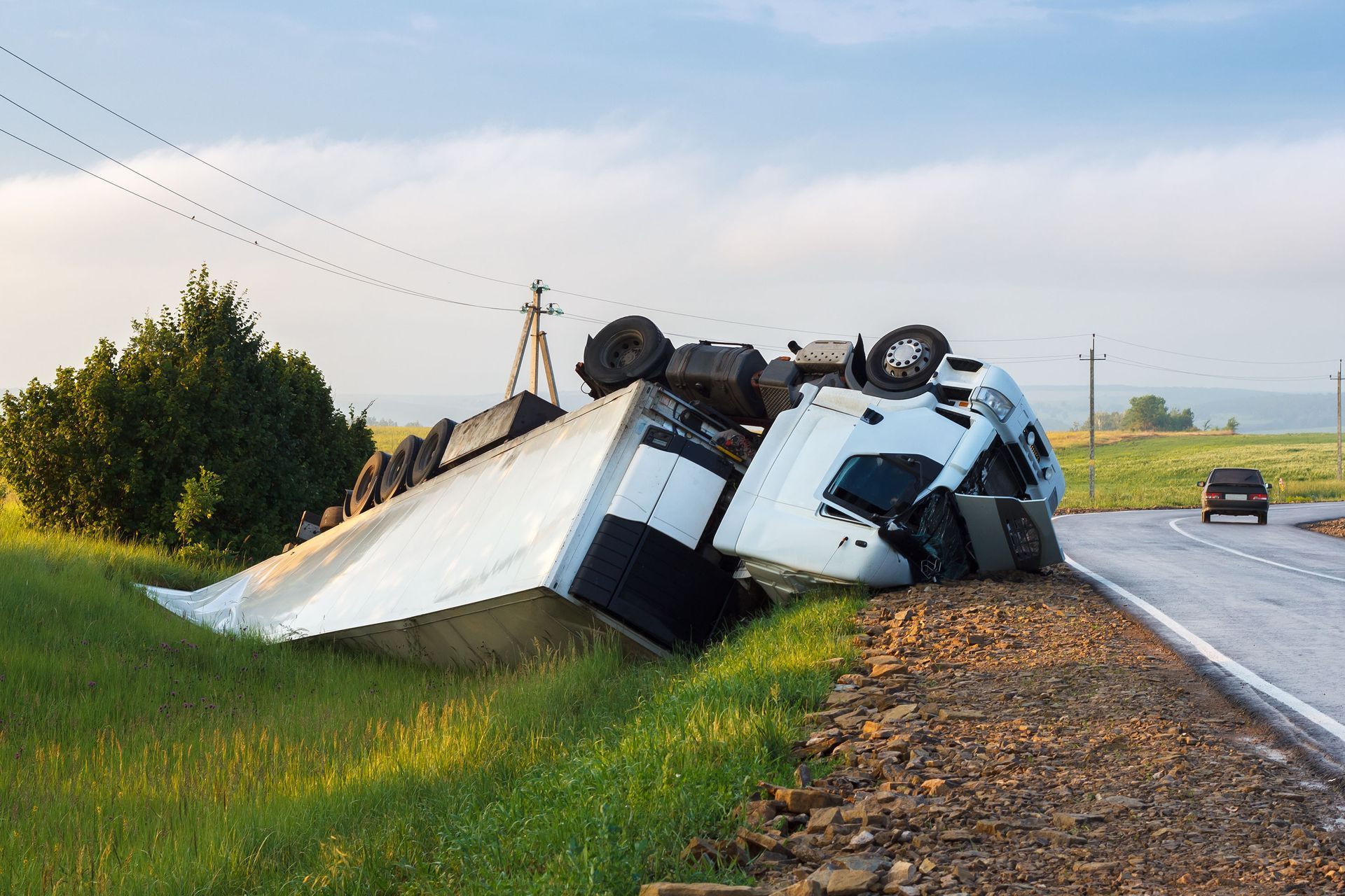 A semi truck has rolled over on its side on the side of the road.