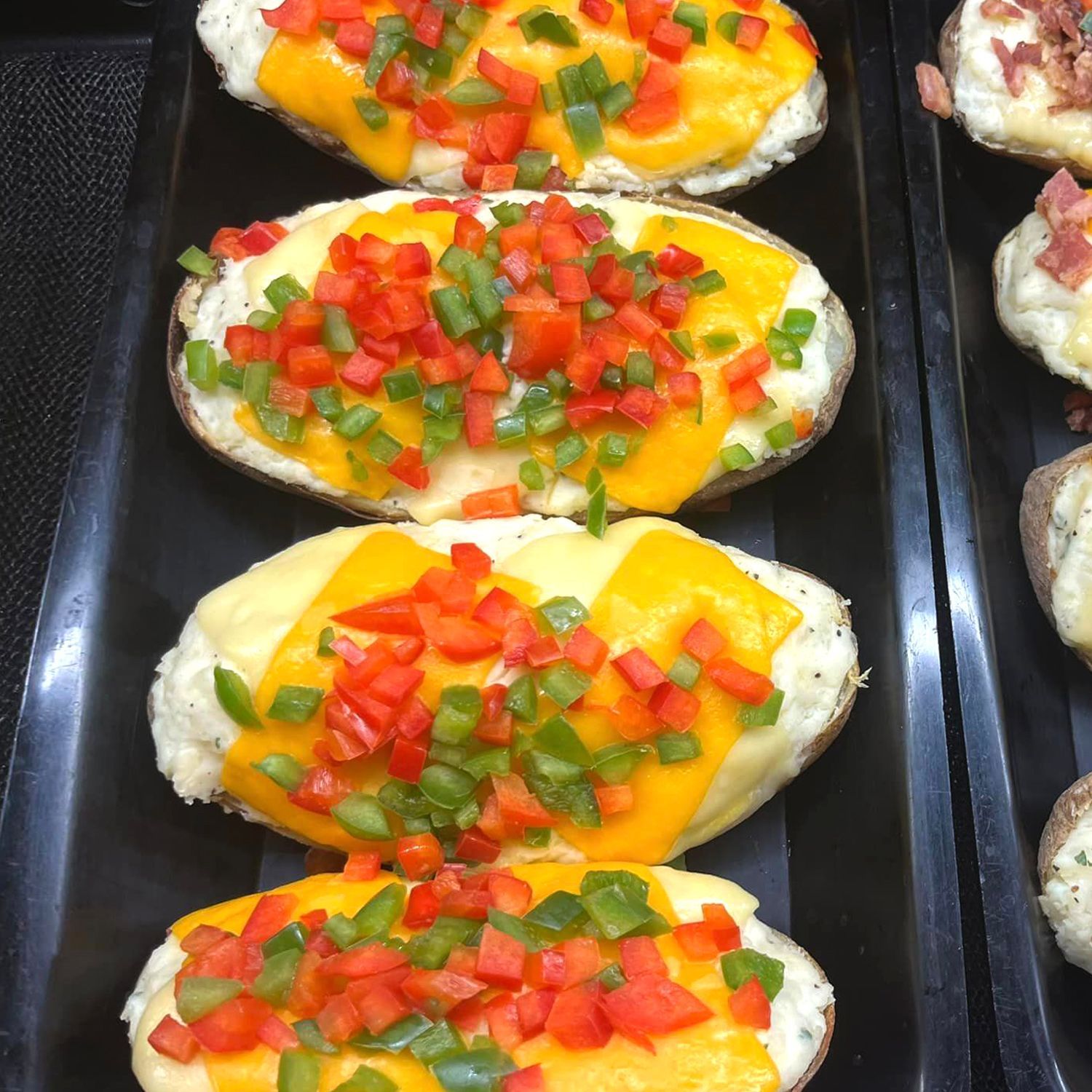A tray of baked potatoes with cheese tomatoes and green onions