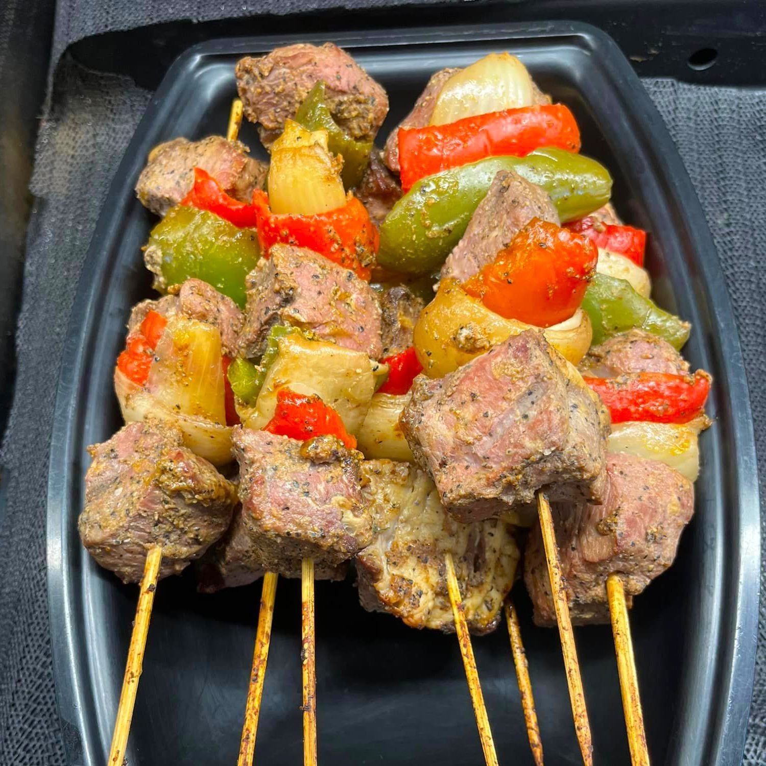 A black plastic container filled with meat and vegetables on skewers