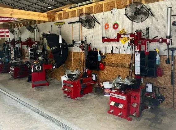 Auto repair shop with red tire machines, tools, and wall-mounted fans along a pegboard wall.