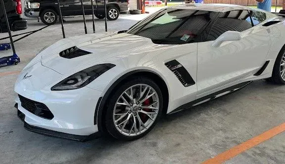 White sports car parked indoors under bright lights, shown from the front-left side.