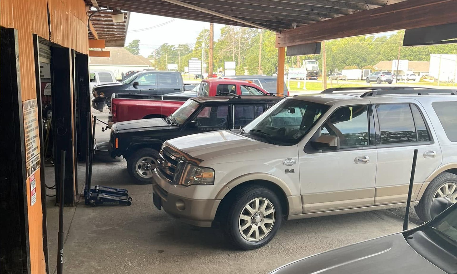 Silver SUV parked under a carport with red and black trucks in the background.