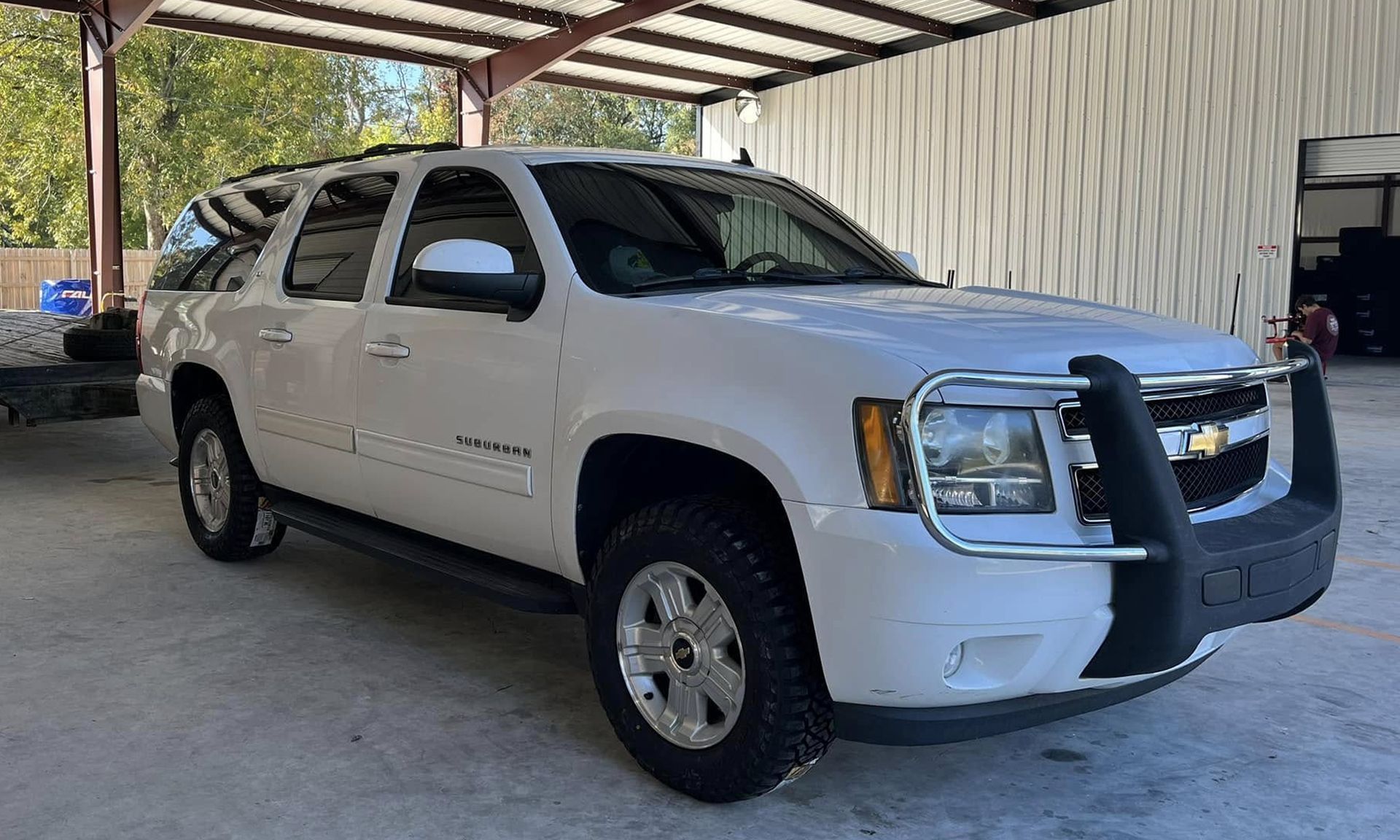 White SUV parked under a metal carport with a black grille guard and tinted windows.