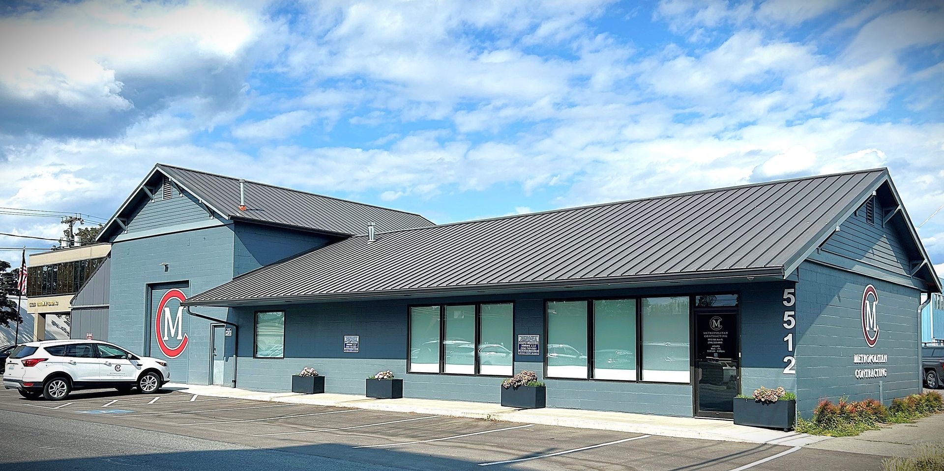 A teal-colored building with a dark roof. A white SUV is parked in front. Blue sky and clouds overhead.