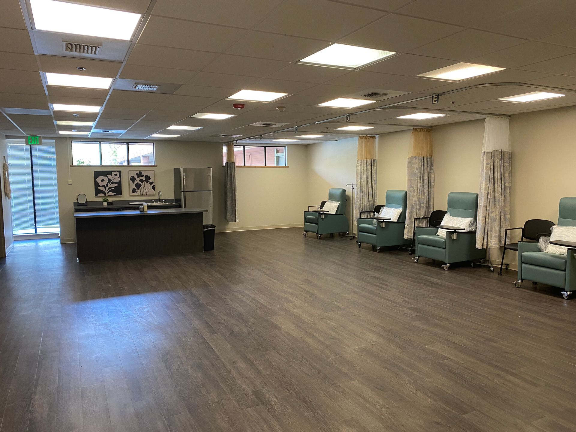 Interior of a medical treatment room with chairs, curtains, and a counter. Neutral colors, bright lighting.