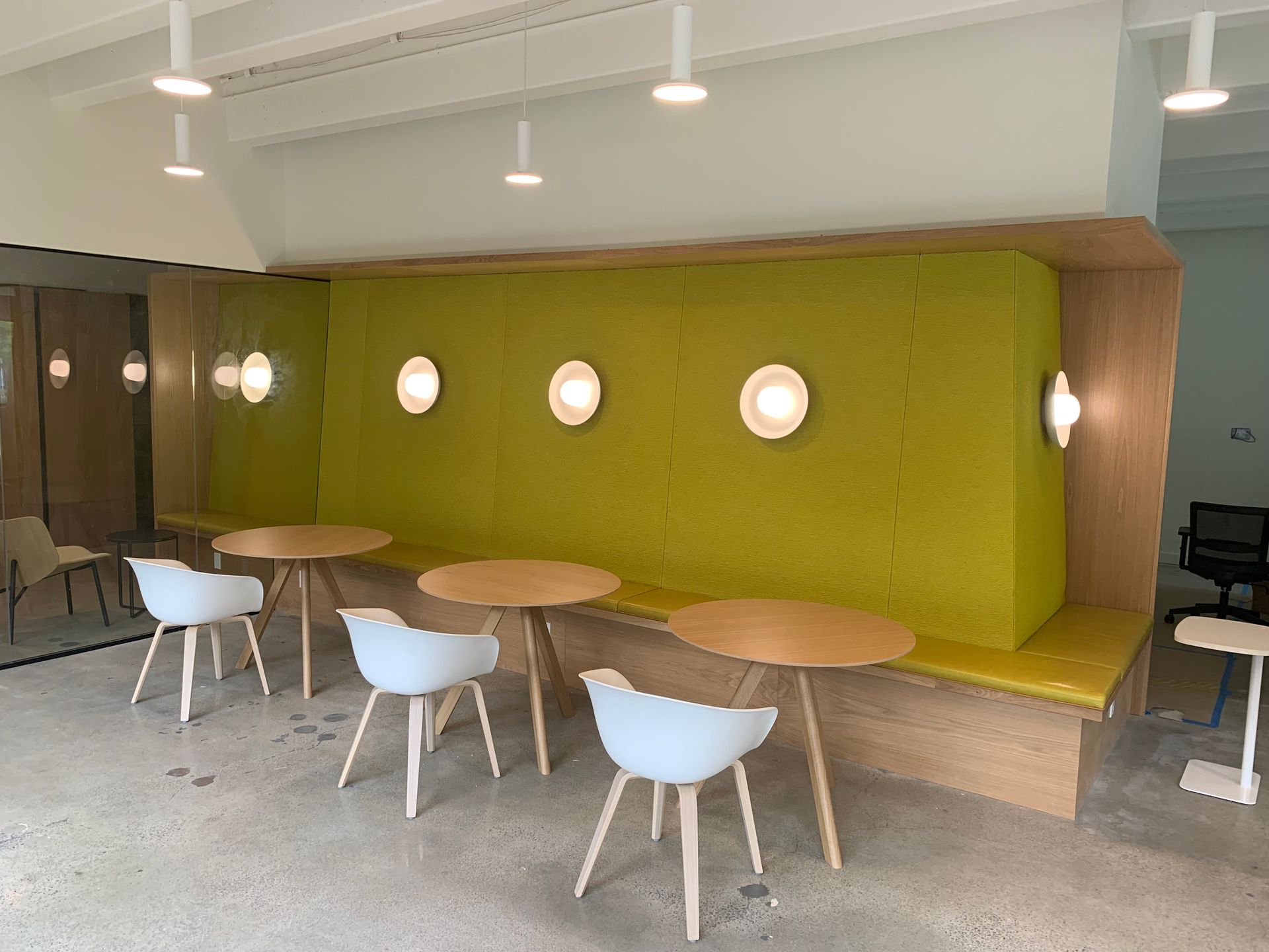 A modern cafe seating area with round tables, white chairs, and a green cushioned booth with wall sconces.