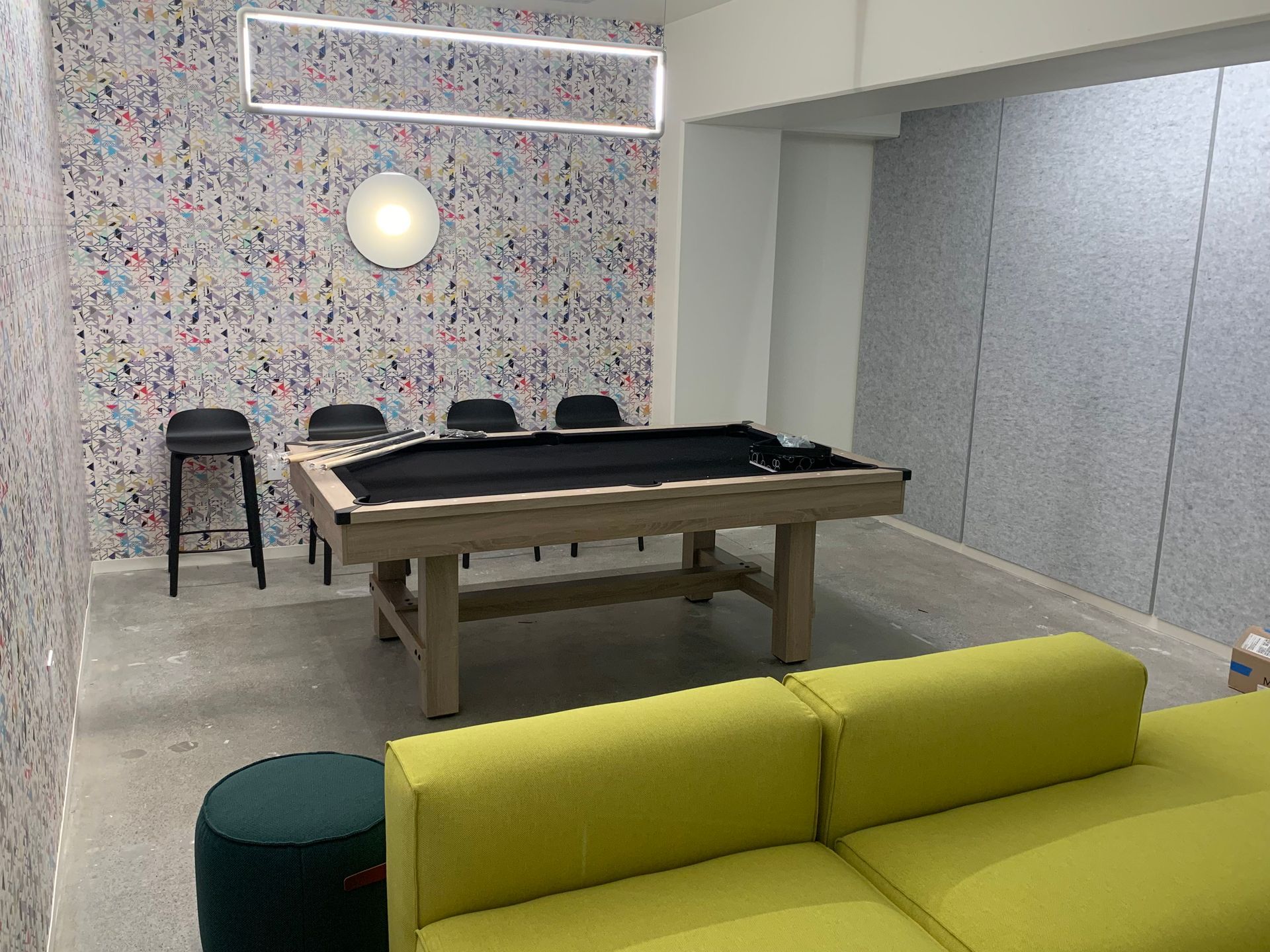 A game room with a pool table, yellow sofa, and colorful textured walls.