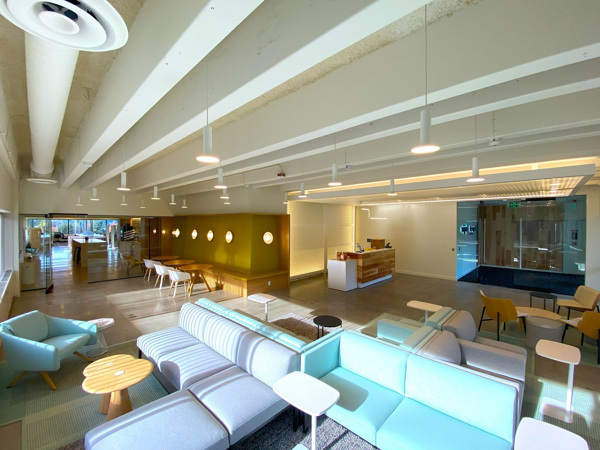 Modern office lobby with light blue and gray seating, wooden accents, and a reception desk.